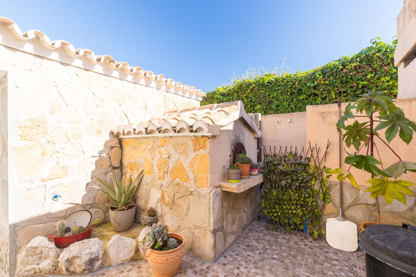 Traditionele houtoven afgewerkt met natuursteen en een pannendak, gelegen op een betegeld terras met diverse vetplanten en mediterrane details.