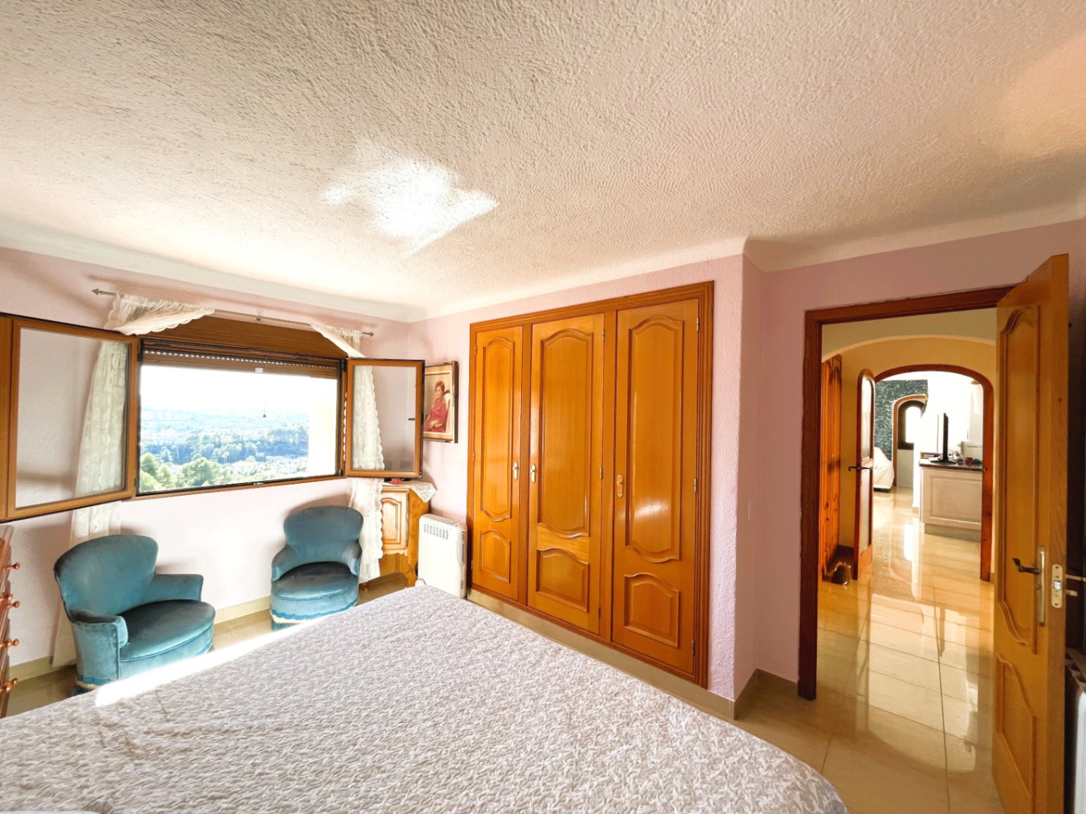 Lichte slaapkamer met ingebouwde houten kasten, fluwelen fauteuils en een raam met weids panoramisch uitzicht over de vallei.