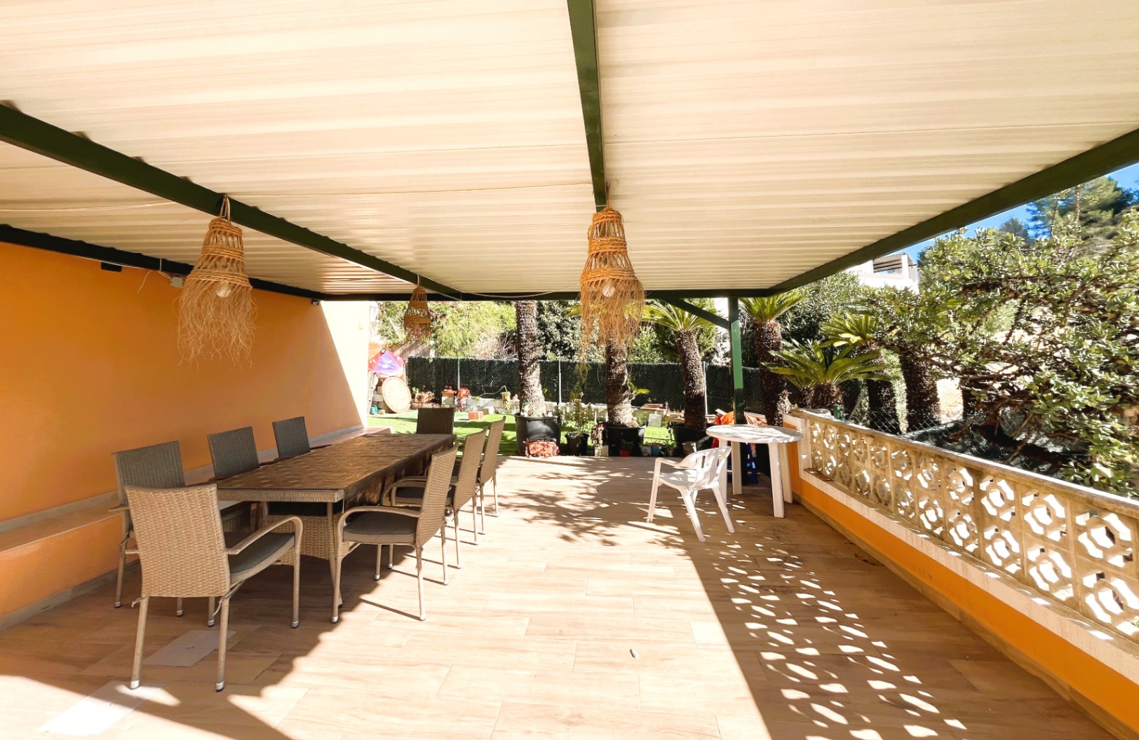 Overdekt terras met een eethoek buiten, rieten hanglampen en een decoratieve balustrade met uitzicht op de mediterrane tuin.