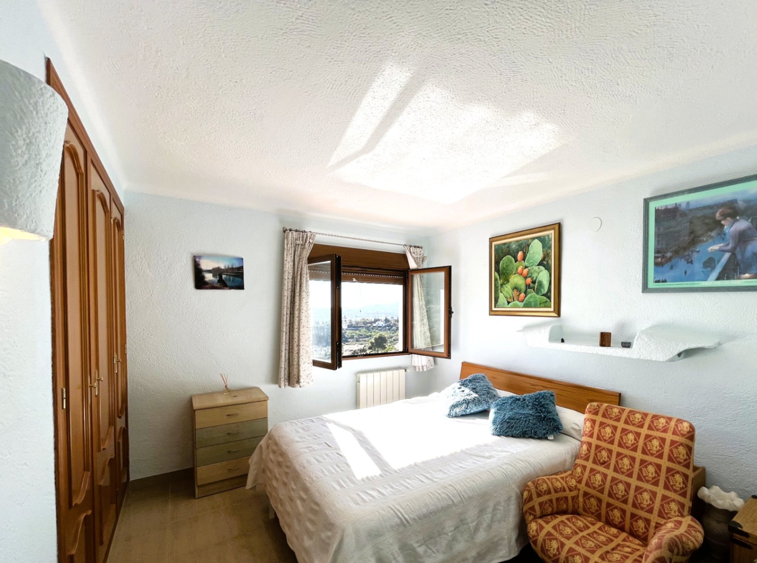 Slaapkamer met ingebouwde houten kasten en een tweepersoonsbed, voorzien van een raam met natuurlijk licht en uitzicht op het omliggende landschap.