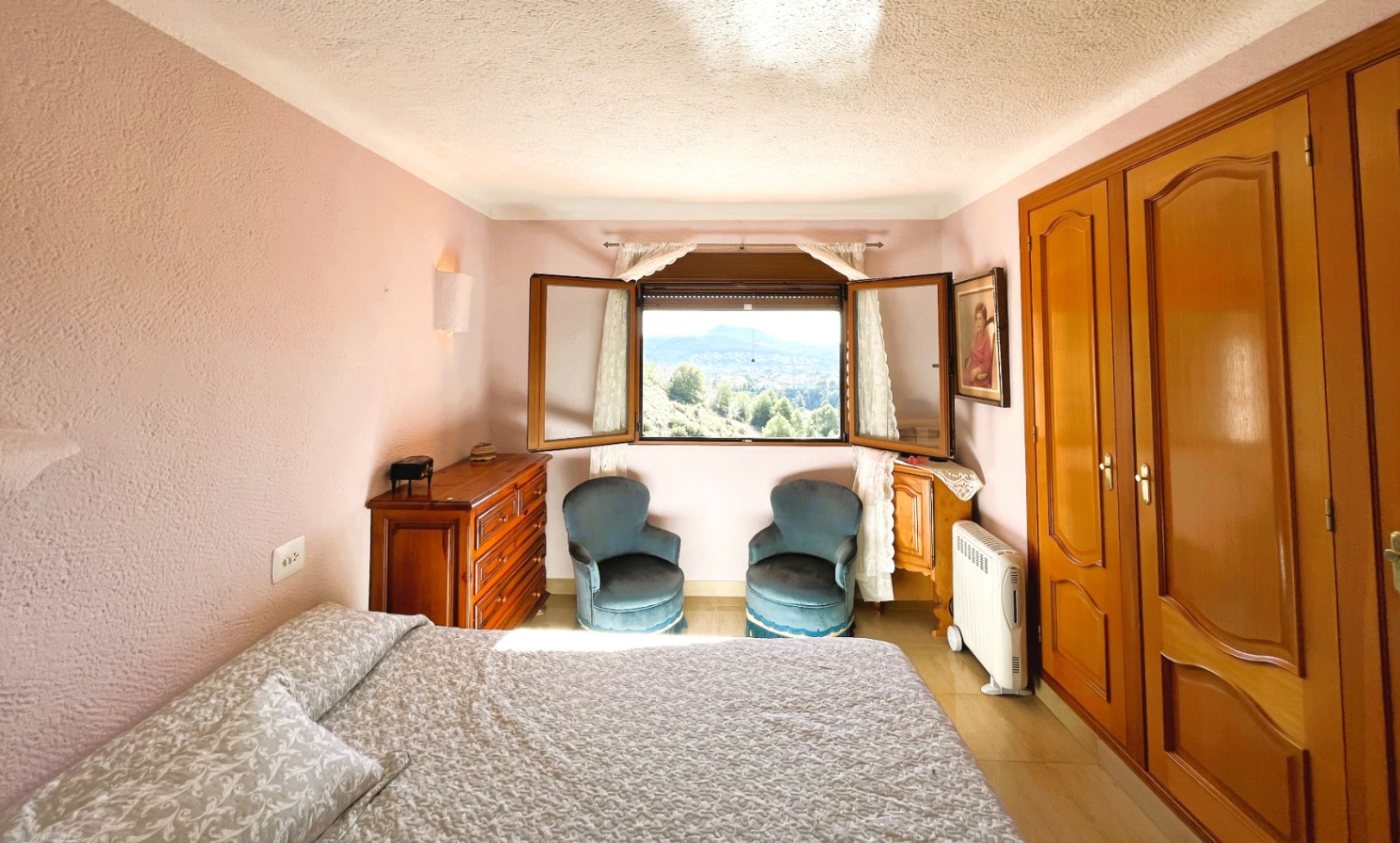Slaapkamer met mauve getextureerde muren, houten inbouwkasten en een raam met panoramisch uitzicht over de vallei en de bergen.
