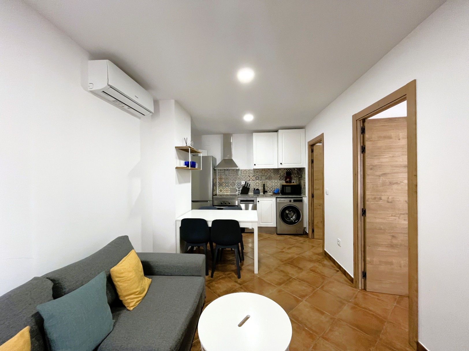 Open woonkamer met moderne keuken, voorzien van een achterwand met patroontegels, airconditioning en een rustieke keramische tegelvloer.