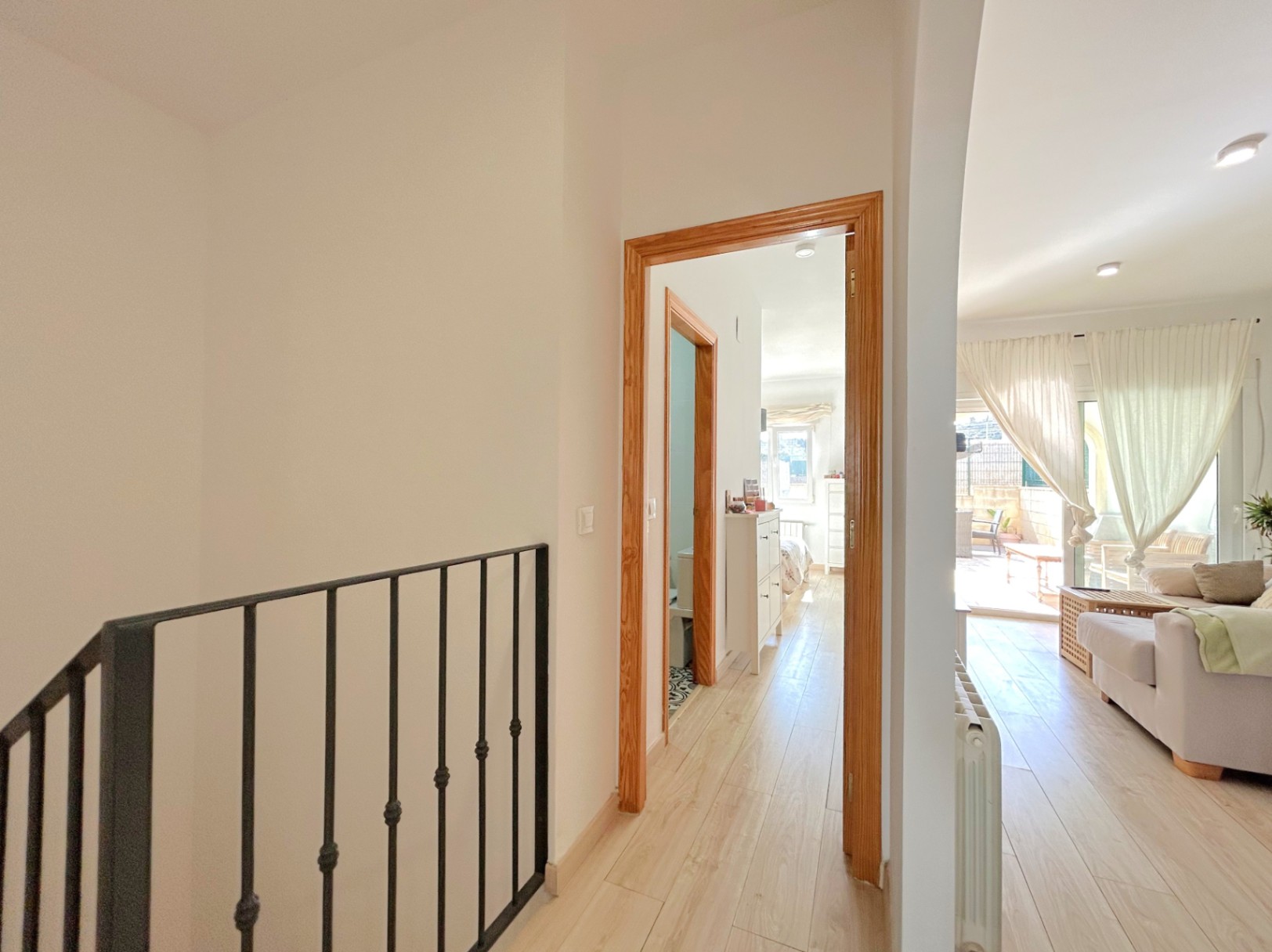 Lichte overloop met houten vloer en smeedijzeren trapleuning die de woonkamer verbindt met de slaapkamers, voorzien van een centrale verwarmingsradiator.