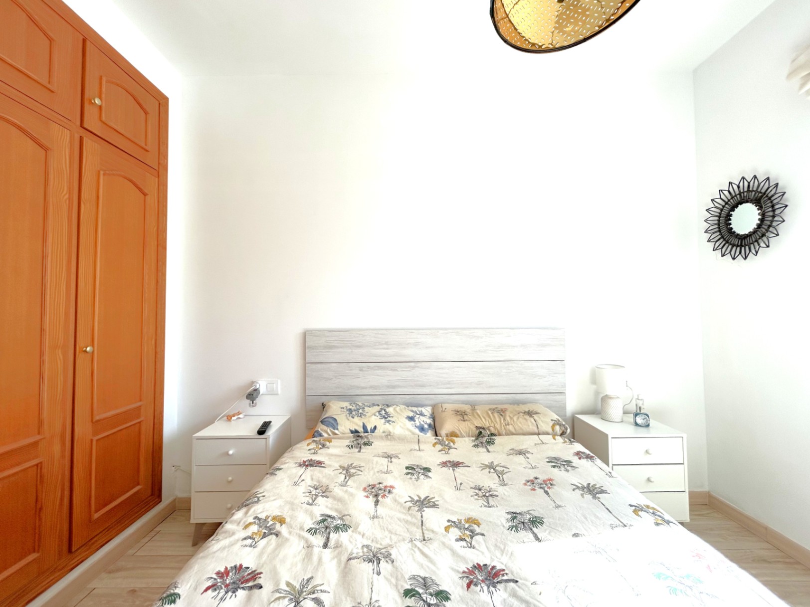 Tweepersoonskamer met ingebouwde houten kledingkast, witte nachtkastjes en een licht houten hoofdbord. De kamer heeft een laminaatvloer en veel natuurlijk licht.