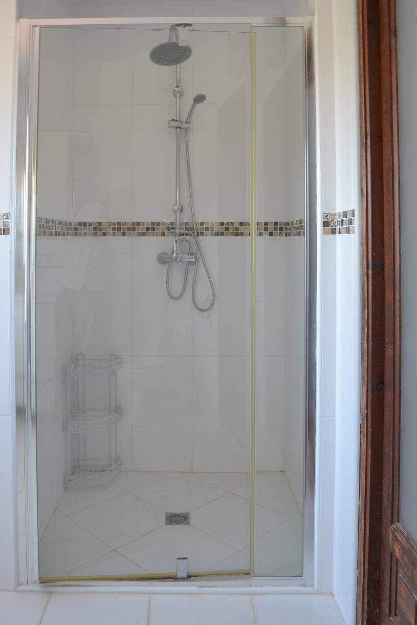 Badkamer met inloopdouche voorzien van een glazen wand, chromen kranen en een regendouche. De witte wandtegels zijn afgewerkt met een decoratieve mozaïekrand.