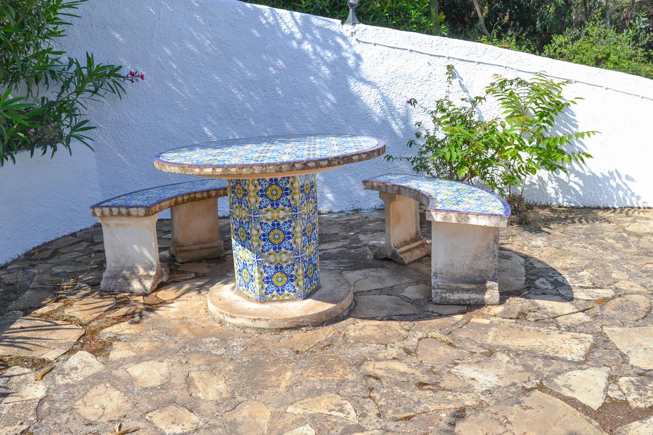 Buiten zithoek met een ronde tafel en gebogen banken gedecoreerd met traditionele blauw-gele tegels, gelegen op een terras van natuursteen.