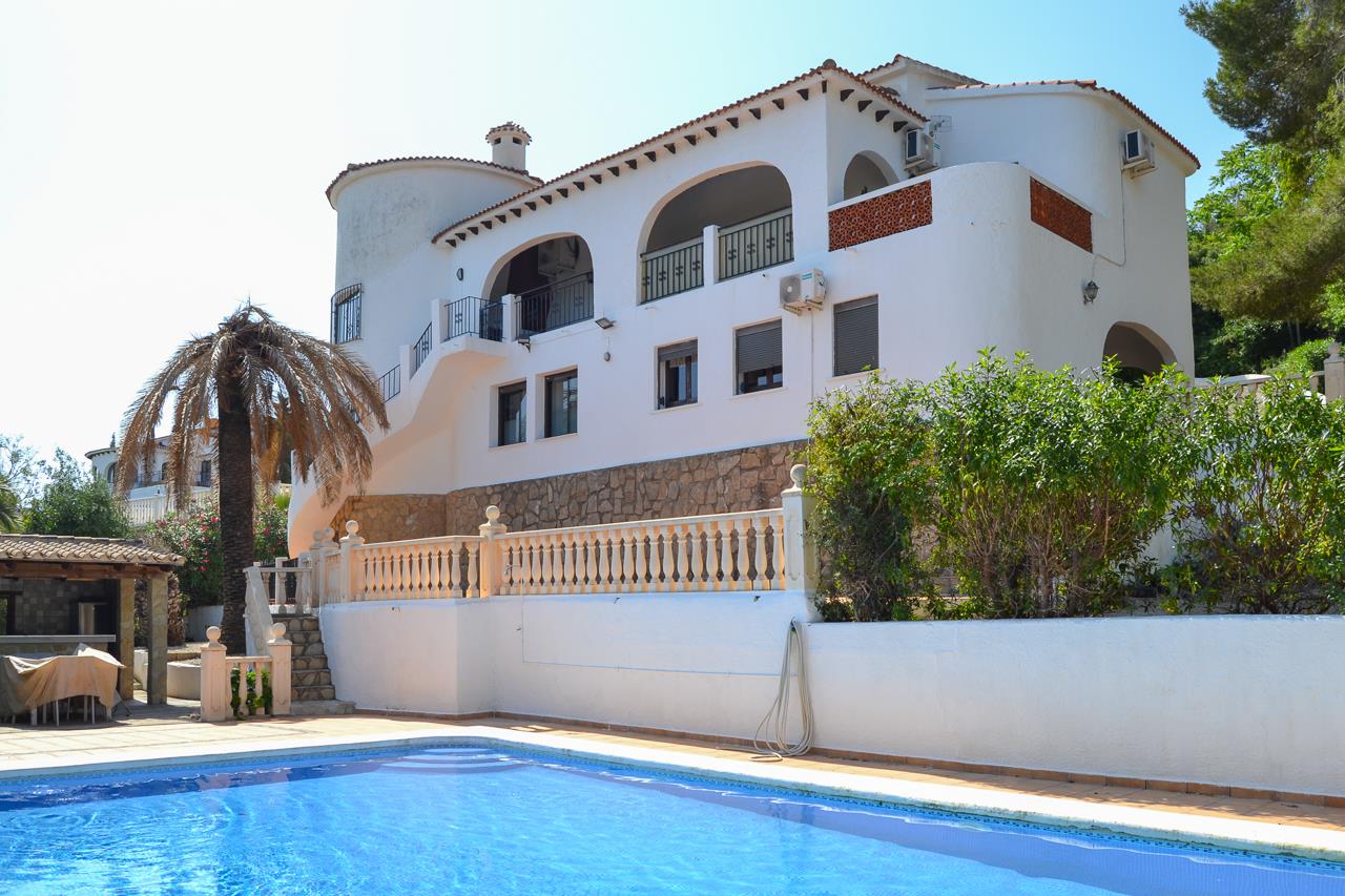Buitenaanzicht van de villa met privézwembad, witte mediterrane gevels en overdekte terrassen met bogen boven een natuurstenen plint.