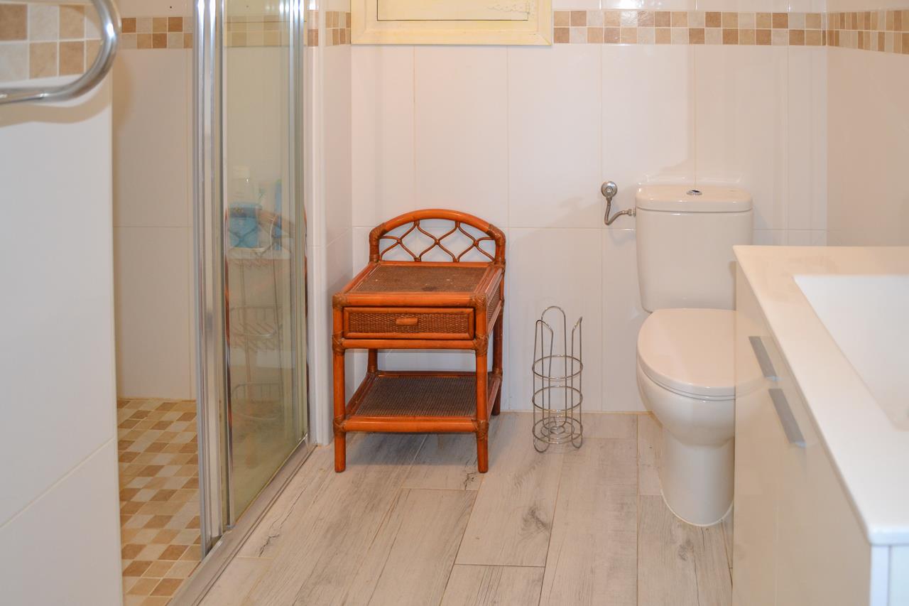 Functionele badkamer met douchecabine, bamboe bijzettafel, keramische vloer met houteffect en wandtegels met een decoratieve mozaïekrand.