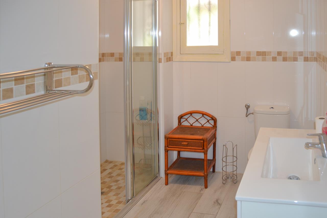 Functionele badkamer met inloopdouche, glazen wand en wit wastafelmeubel. Voorzien van lichte tegels met een decoratieve rand en natuurlijke lichtinval.