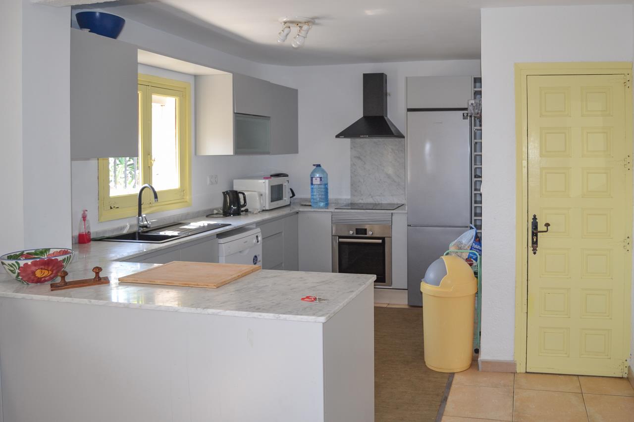 Functionele keuken met marmeren werkbladen, lichtgrijze kasten en inbouwapparatuur. Het gele raamkozijn en de bijpassende deur zorgen voor een helder kleuraccent.