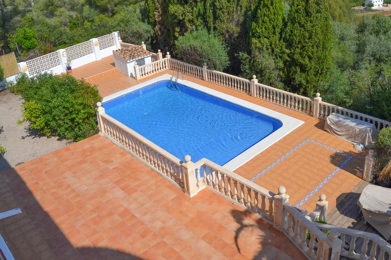 Groot rechthoekig zwembad met een terras van terracotta tegels en een klassieke stenen balustrade, omgeven door een volgroeide mediterrane tuin.