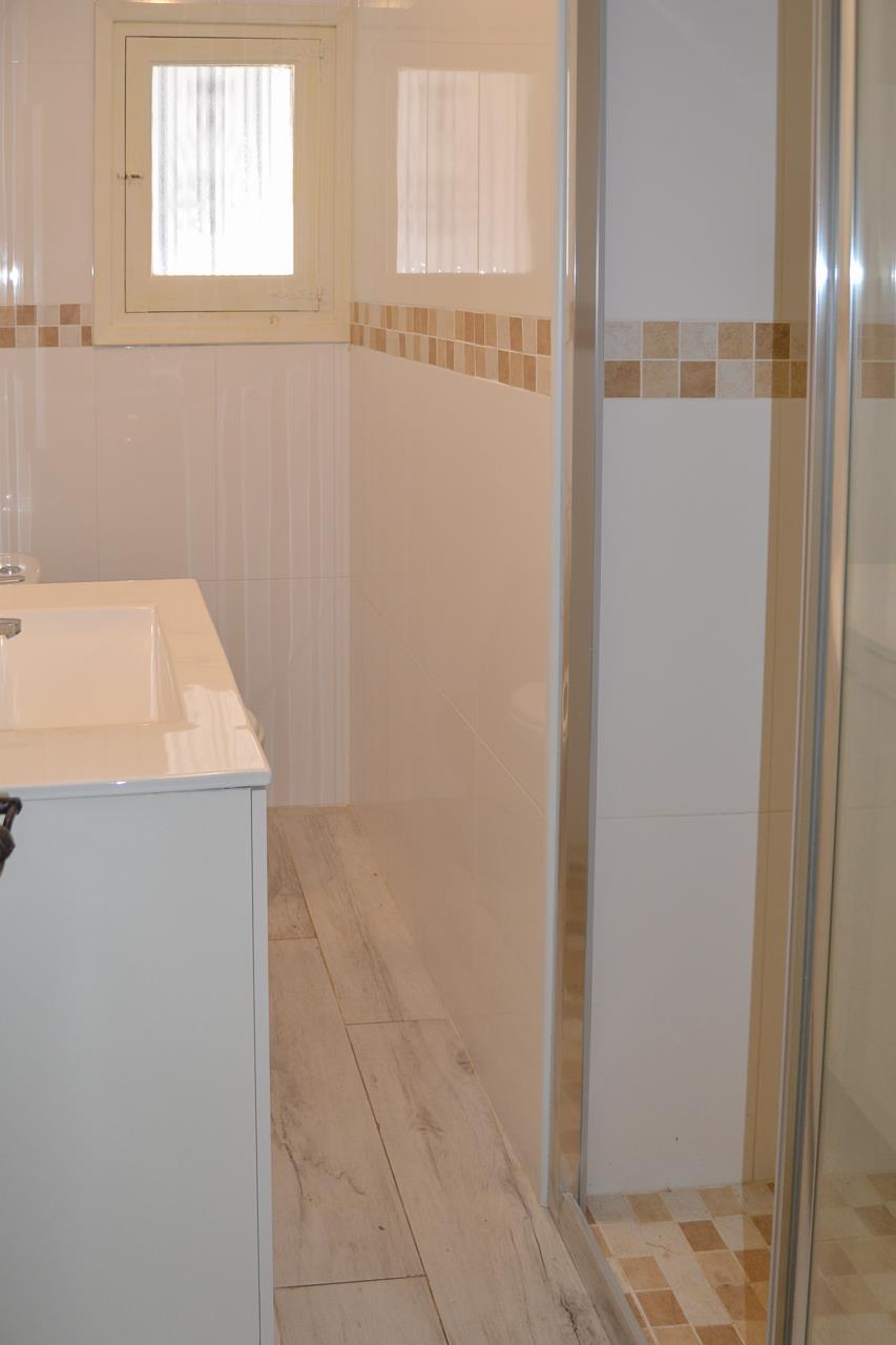Moderne badkamer met wit wastafelmeubel, betegelde wanden met mozaïekrand en een glazen douchecabine met bijpassende vloertegels.