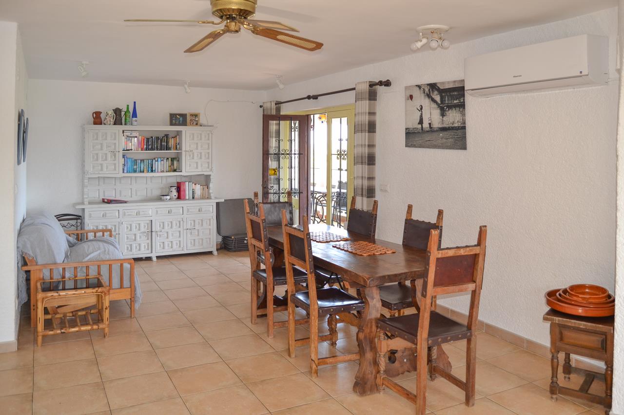 Rustieke eethoek met massief houten tafel, stoelen met hoge rugleuning, wit dressoir en tegelvloer. Voorzien van airconditioning, plafondventilator en toegang tot het terras.