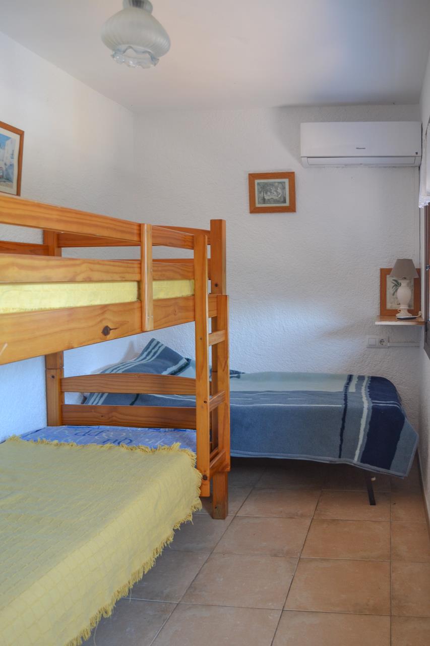 Slaapkamer met grenenhouten stapelbed en een extra eenpersoonsbed. Voorzien van airconditioning, een tegelvloer en witte muren met textuur.