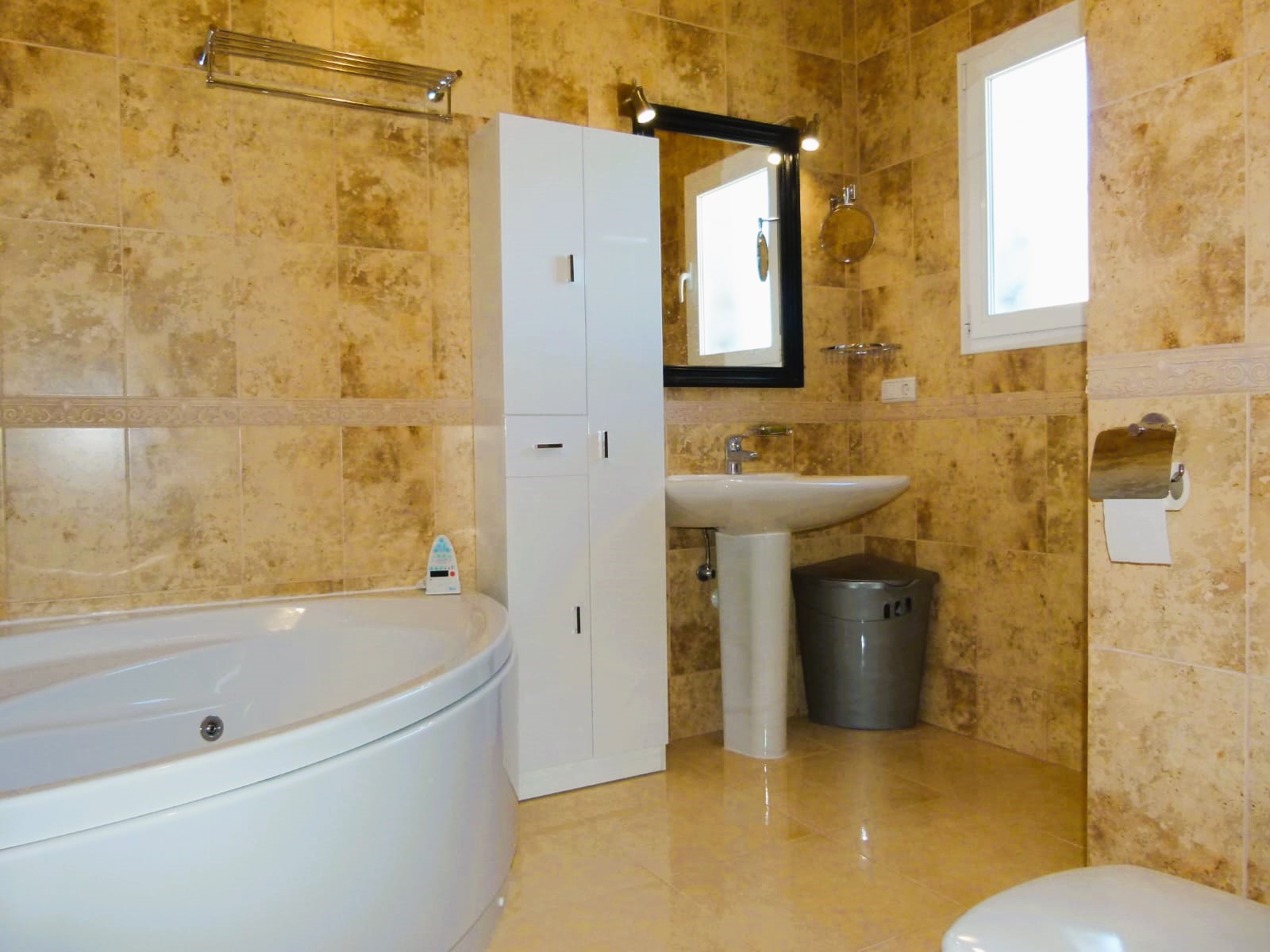 Badkamer met rond bad, wastafel op voetstuk en beige tegels.