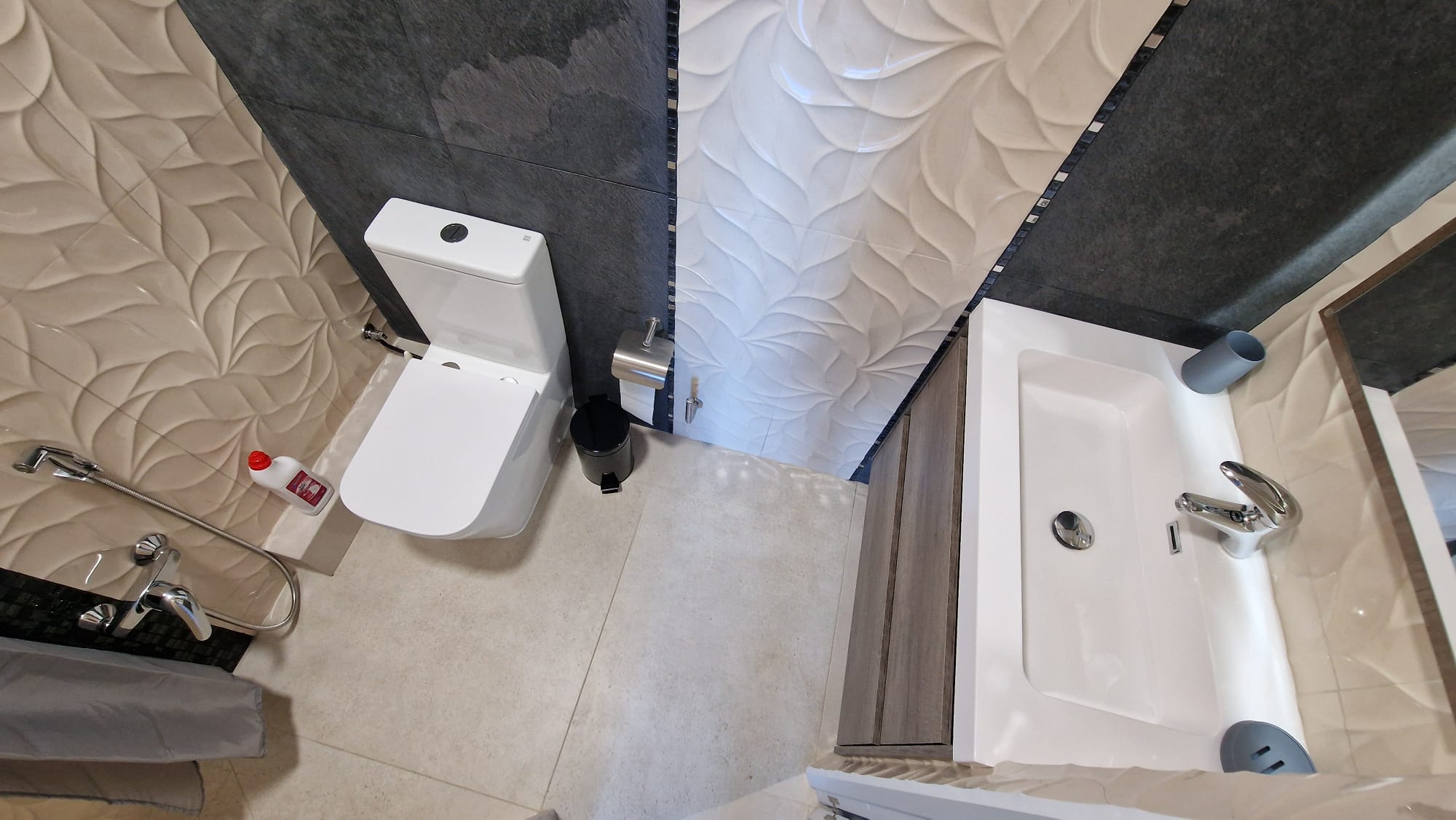 Badkamerdetail met getextureerde tegels, een wit toilet en een moderne wastafel. Functioneel en elegant ontwerp.