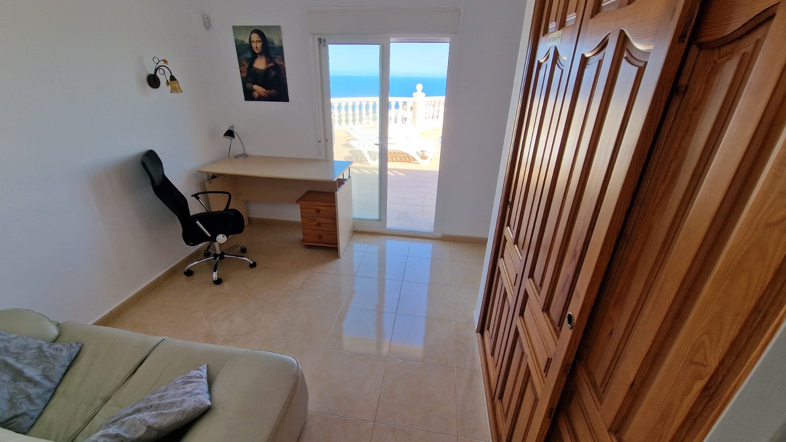Lichte kamer met bureau, houten kledingkast en toegang tot het terras met uitzicht op zee.