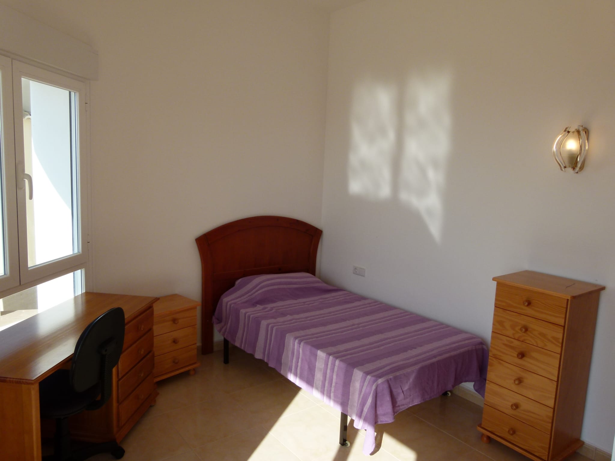 Lichte slaapkamer met eenpersoonsbed, houten bureau en bijpassende ladekast.