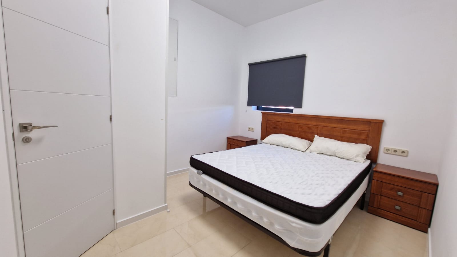 Lichte slaapkamer met tweepersoonsbed, houten nachtkastjes en een moderne witte deur.