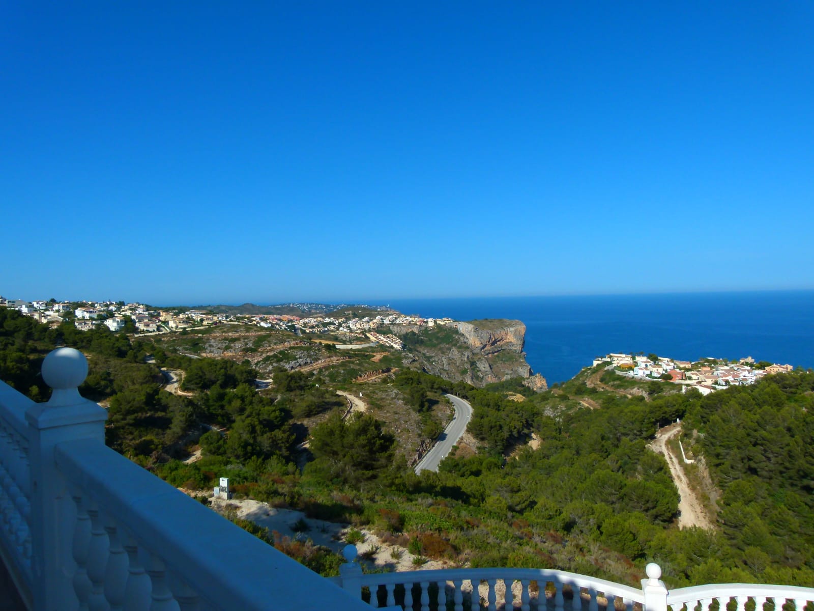Panoramisch uitzicht vanaf het terras met witte balustrade richting de kust en de blauwe zee.