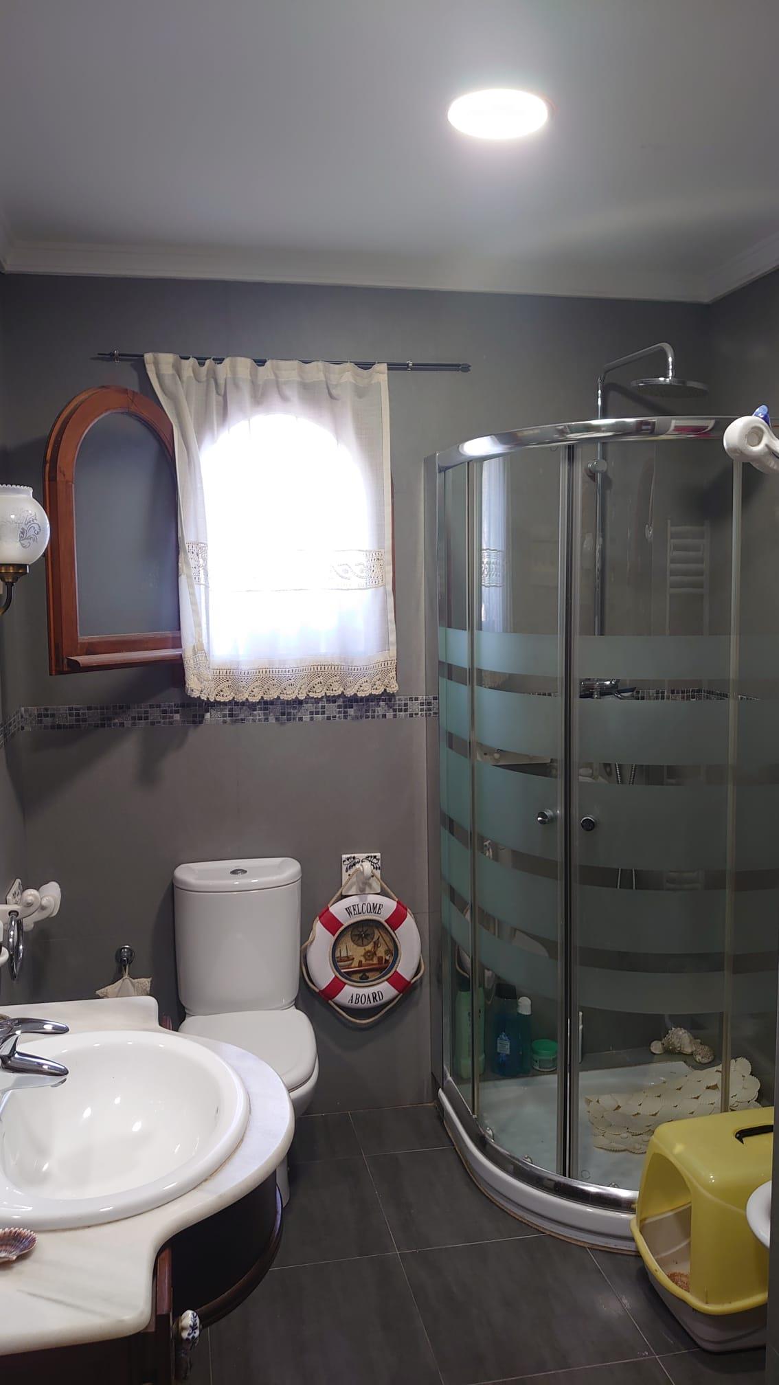 Badkamer met een glazen hoekdouche, grijze wanden en een marmeren wastafelblad. Voorzien van een houten boograam en decoratieve nautische accenten.