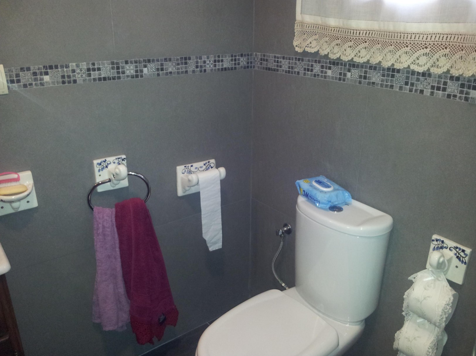 Badkamer met grijze wandtegels en mozaïekrand, voorzien van een wit toilet en keramische accessoires met blauwe bloemmotieven.