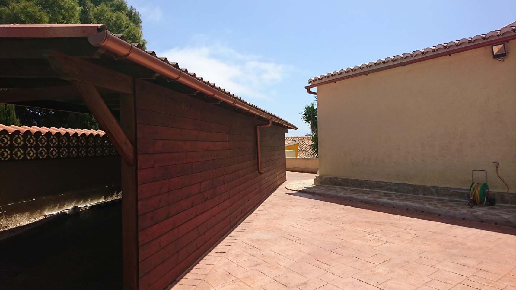 Bestraat buitenterrein met een houten carport en een traditionele gevel, afgewerkt met terracotta dakpannen en koperen dakgoten.