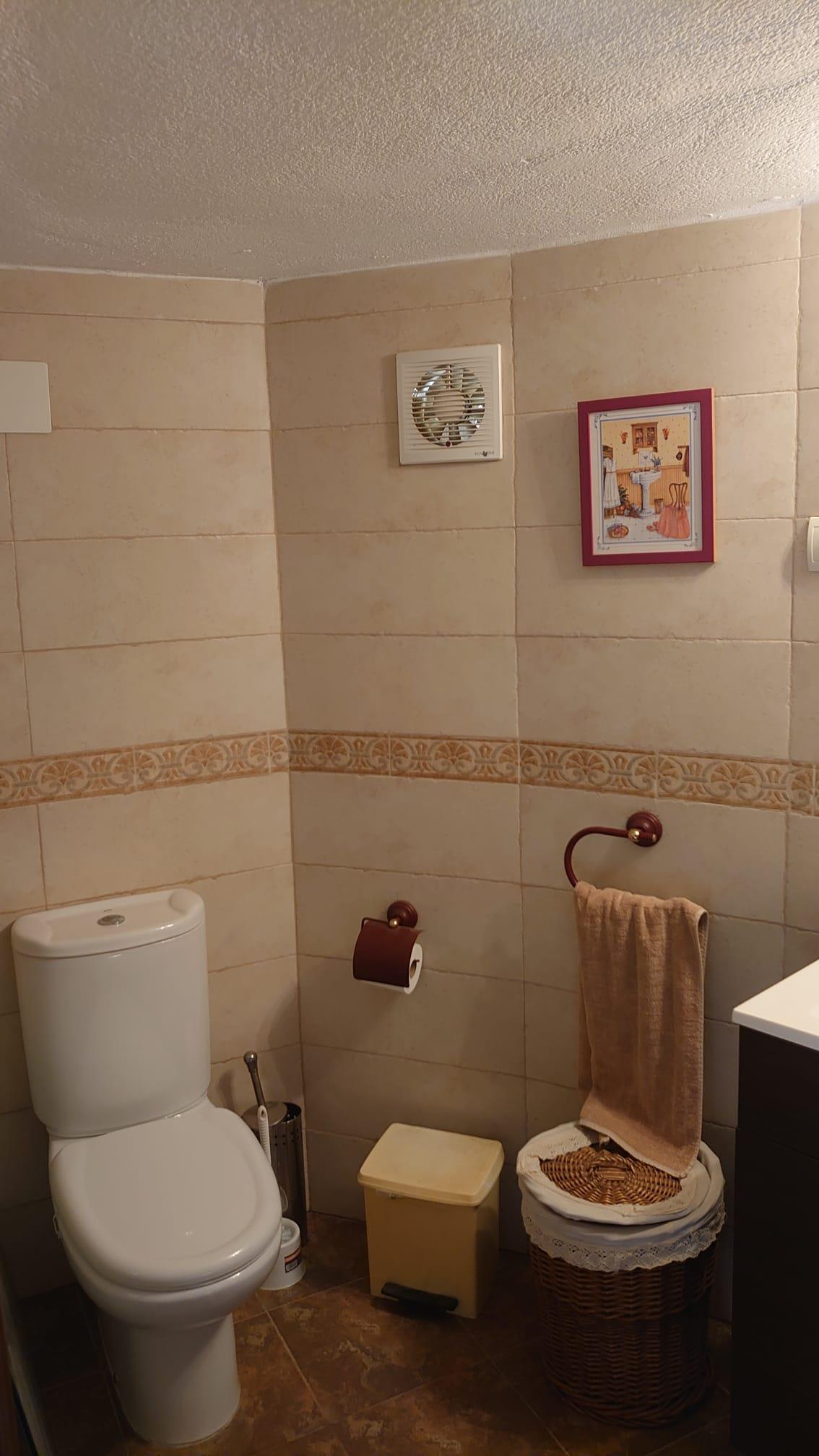 Functionele badkamer met crèmekleurige tegels, een sierrand en wit sanitair. Voorzien van donkerhouten accessoires en een klassieke rieten mand.