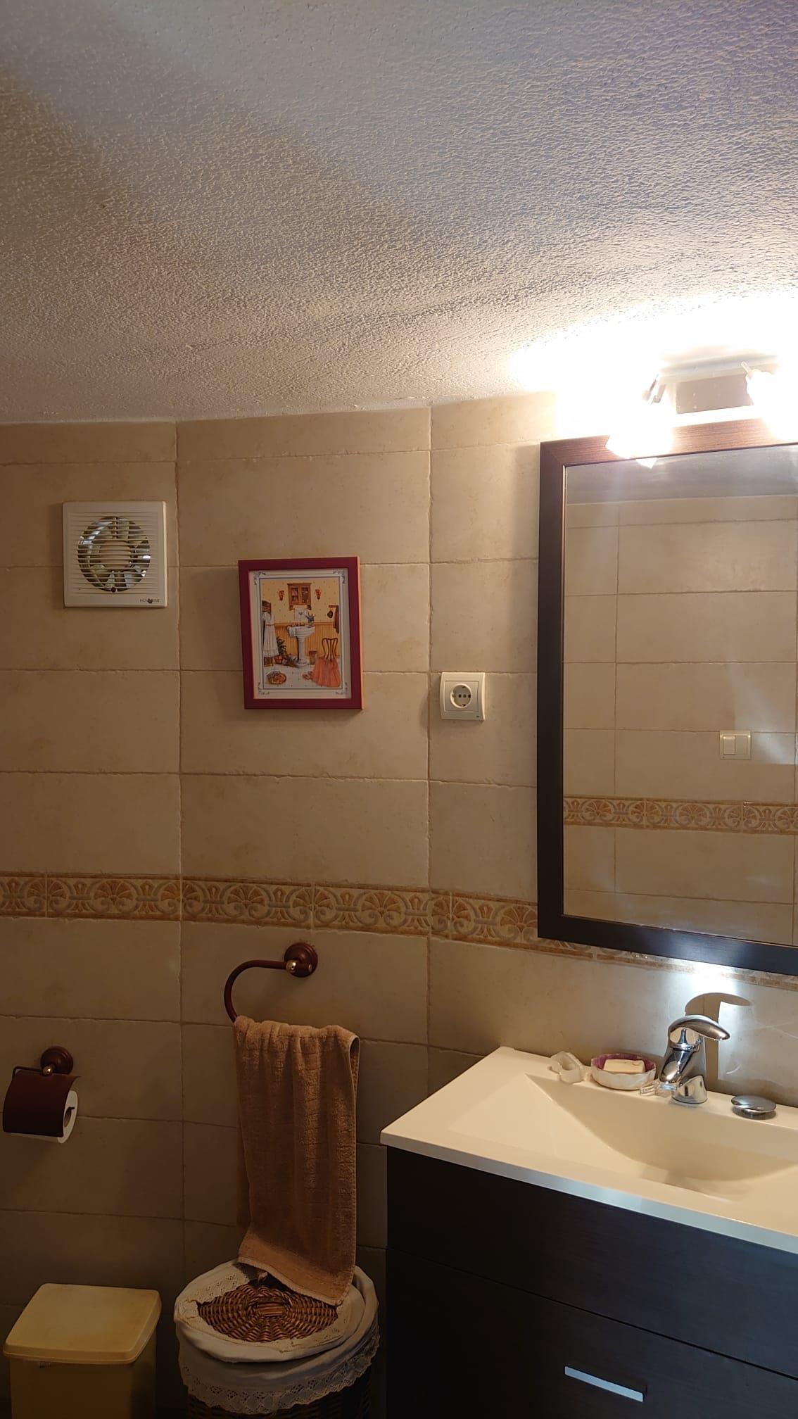 Functionele badkamer met een donker wastafelmeubel, ingelijste spiegel en beige wandtegels voorzien van een decoratieve sierrand en afzuiging.