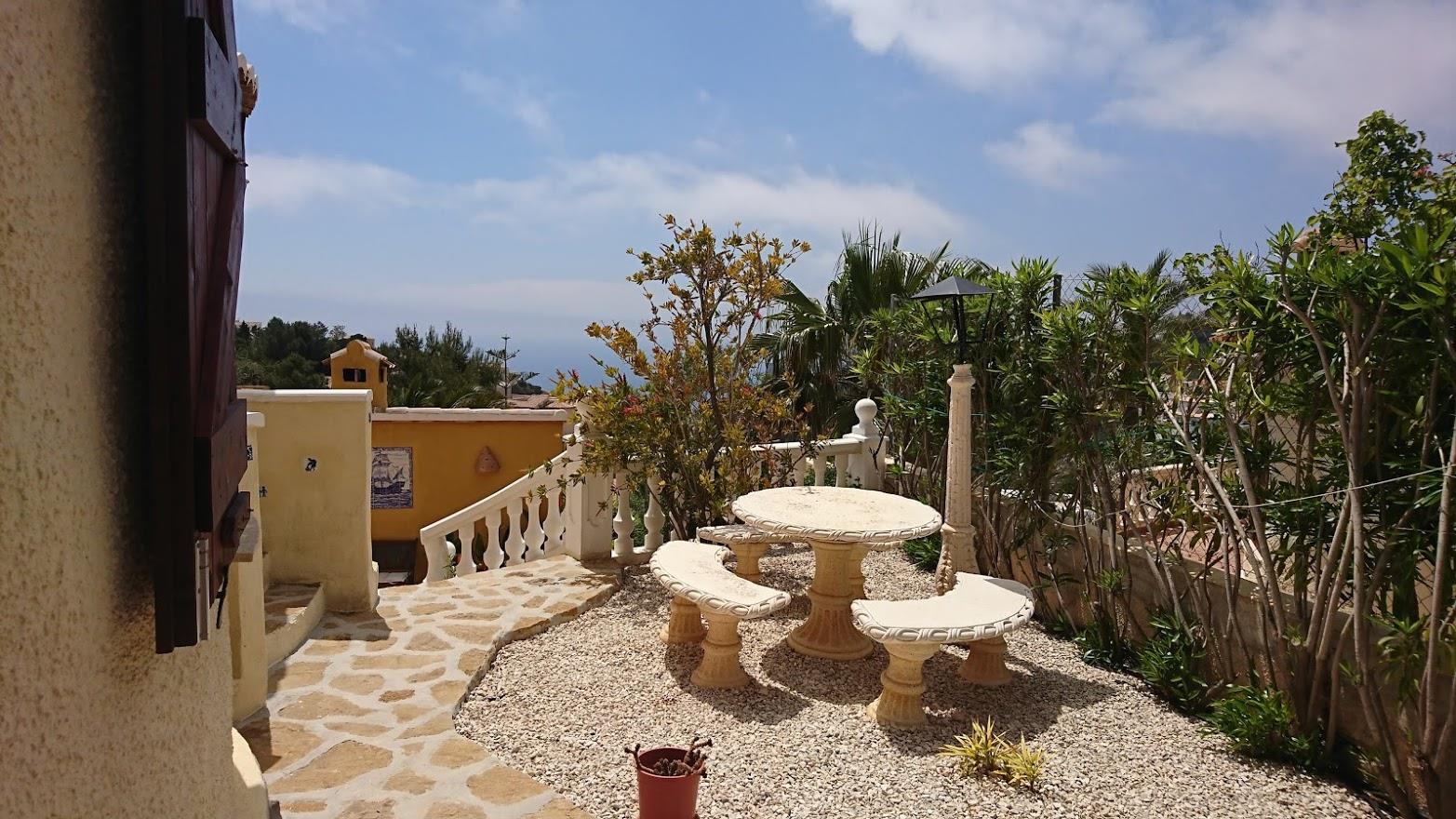 Grindterras met een stenen tafelset en banken, omgeven door mediterrane vegetatie en een witte balustrade met uitzicht op de Middellandse Zee.