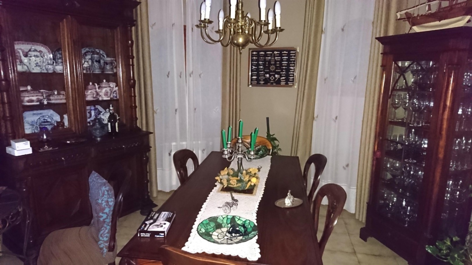 Klassieke eetkamer met een massief houten tafel, sierlijke vitrinekasten voor servies en een koperen kroonluchter boven een kanten tafelloper.
