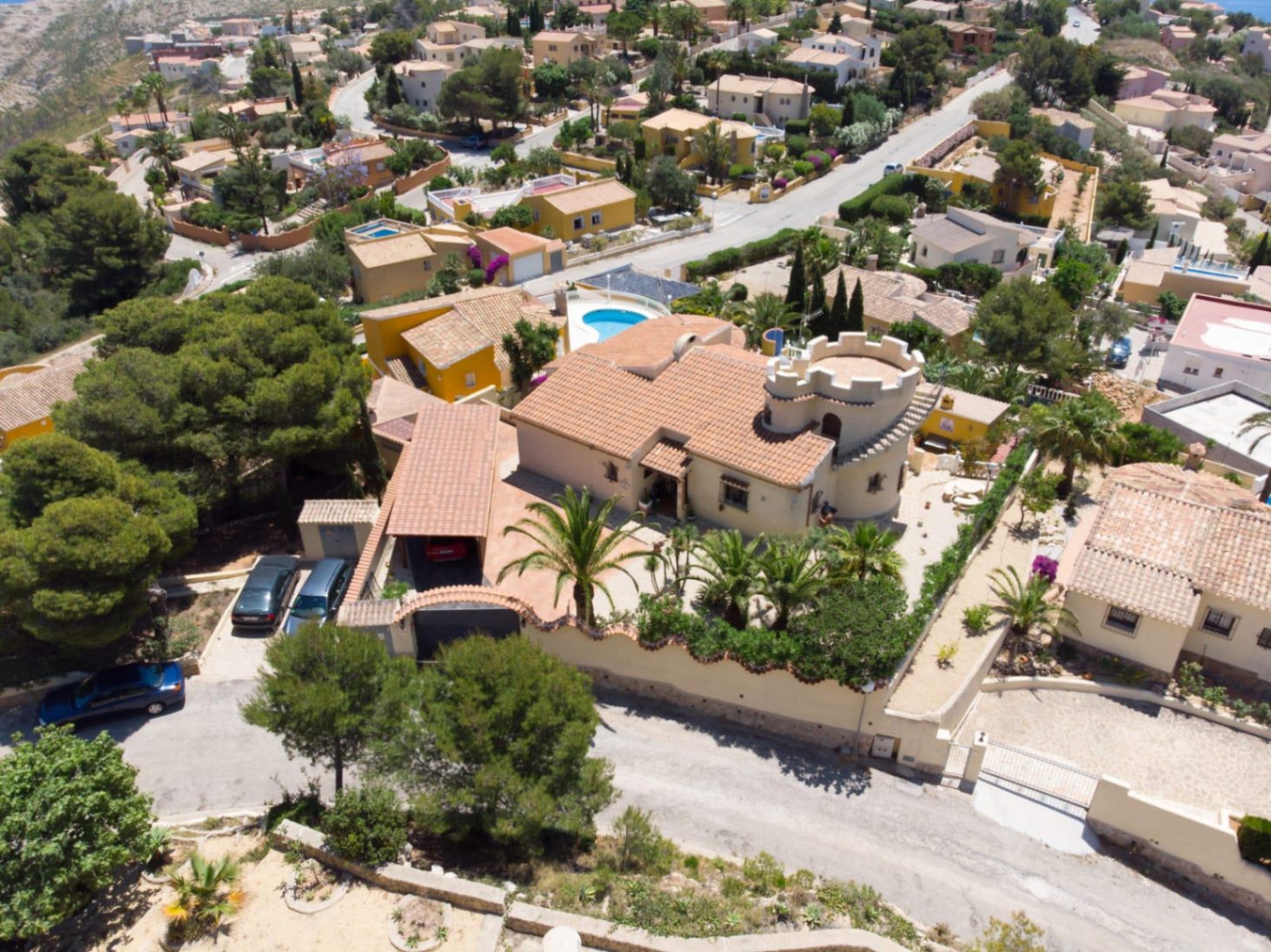 Luchtfoto van de villa met een kenmerkende toren met kantelen, een pannendak en een mediterrane tuin met palmbomen op een verhoogd perceel.