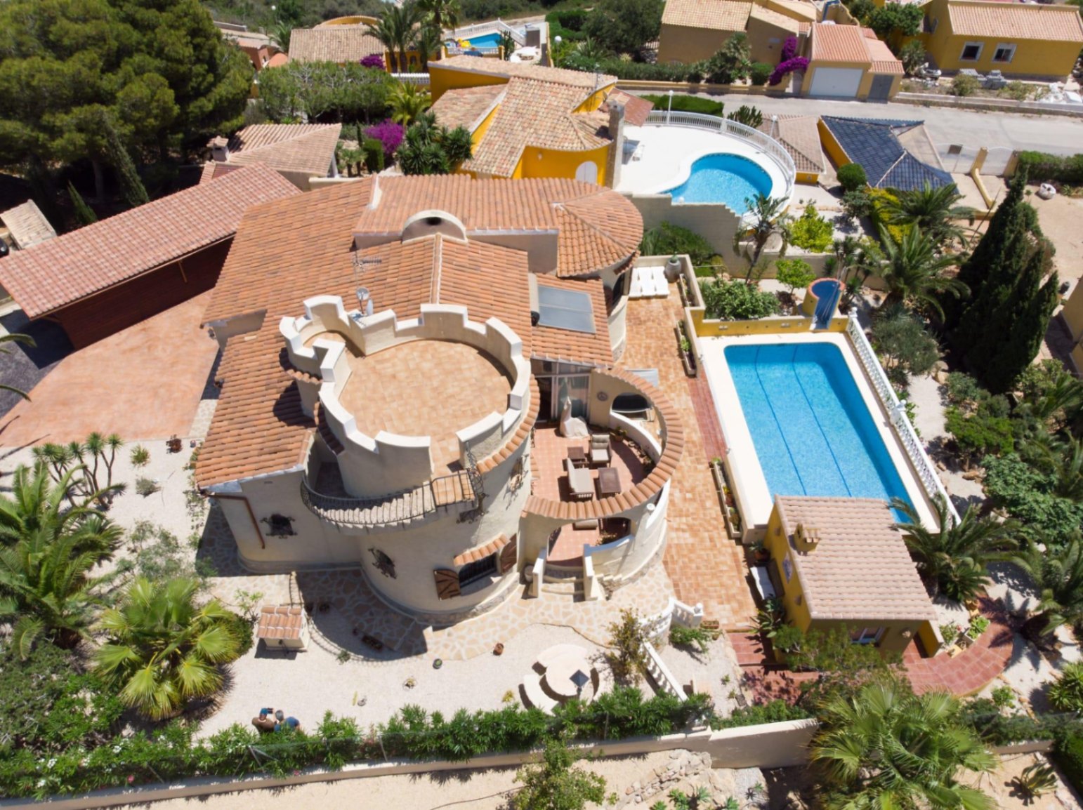 Luchtfoto van de villa met mediterrane architectuur, een ronde toren, terracotta daken, een rechthoekig zwembad en een vrijstaande buitenkeuken in de tuin.