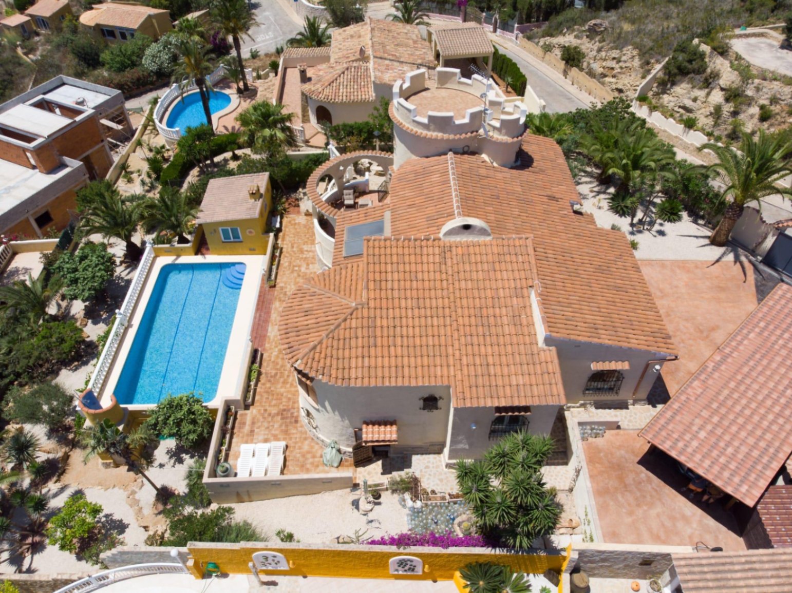 Luchtfoto van de villa met mediterrane architectuur, terracotta daken, een karakteristieke toren met kantelen en een rechthoekig zwembad omgeven door tuinen.