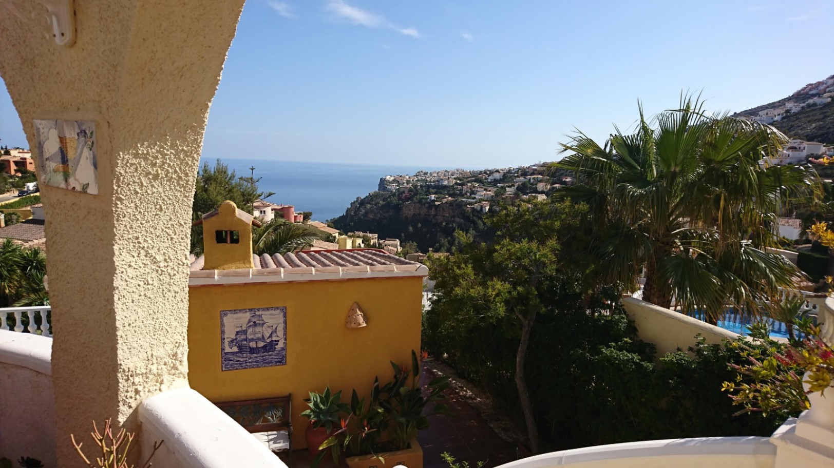 Panoramisch uitzicht op de Middellandse Zee door een traditionele boog, met decoratieve tegels en volwassen mediterrane beplanting.
