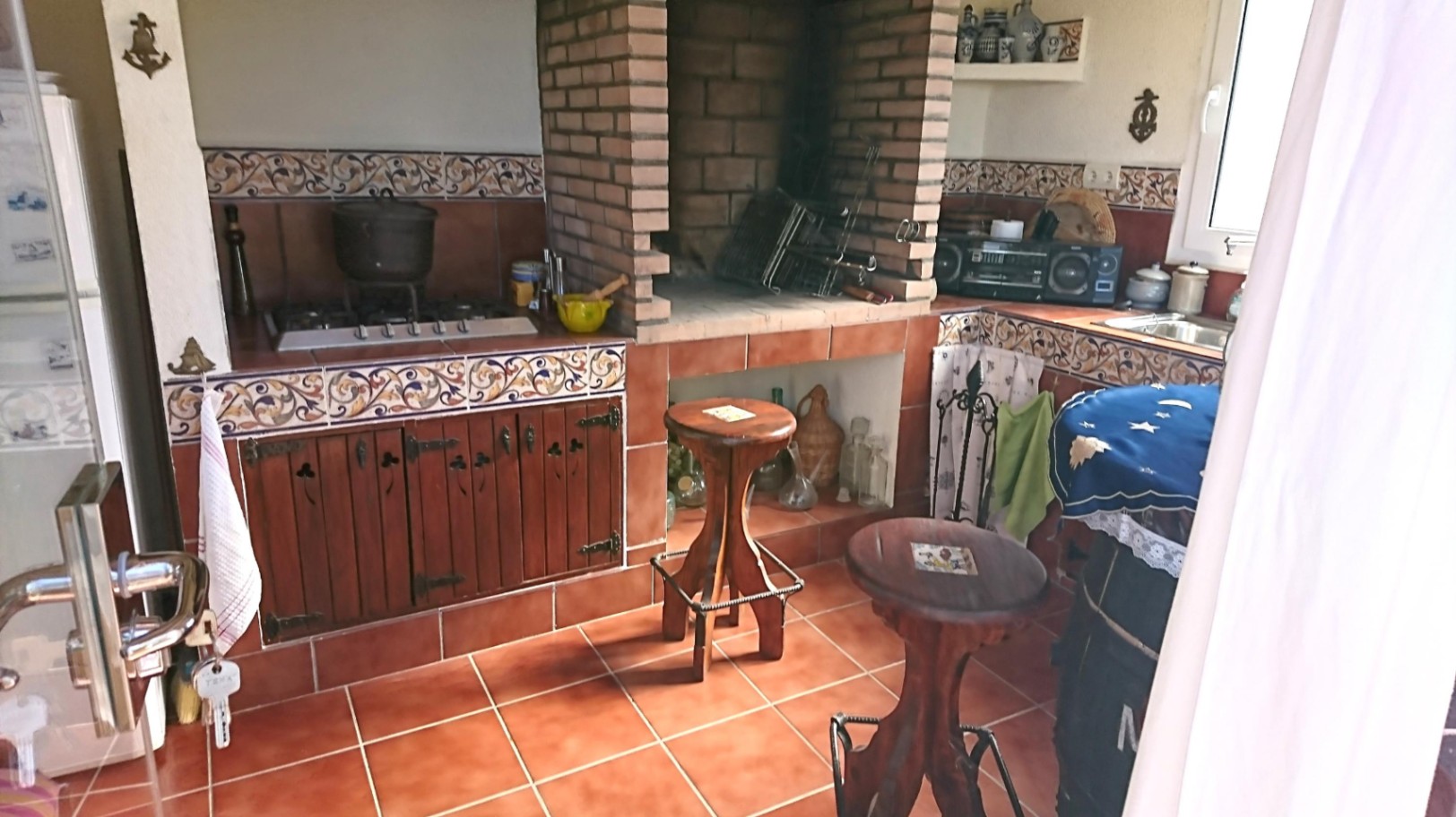 Rustieke zomerkeuken met een ingebouwde bakstenen barbecue, decoratieve tegelwanden, houten kasten en traditionele terracotta vloeren.