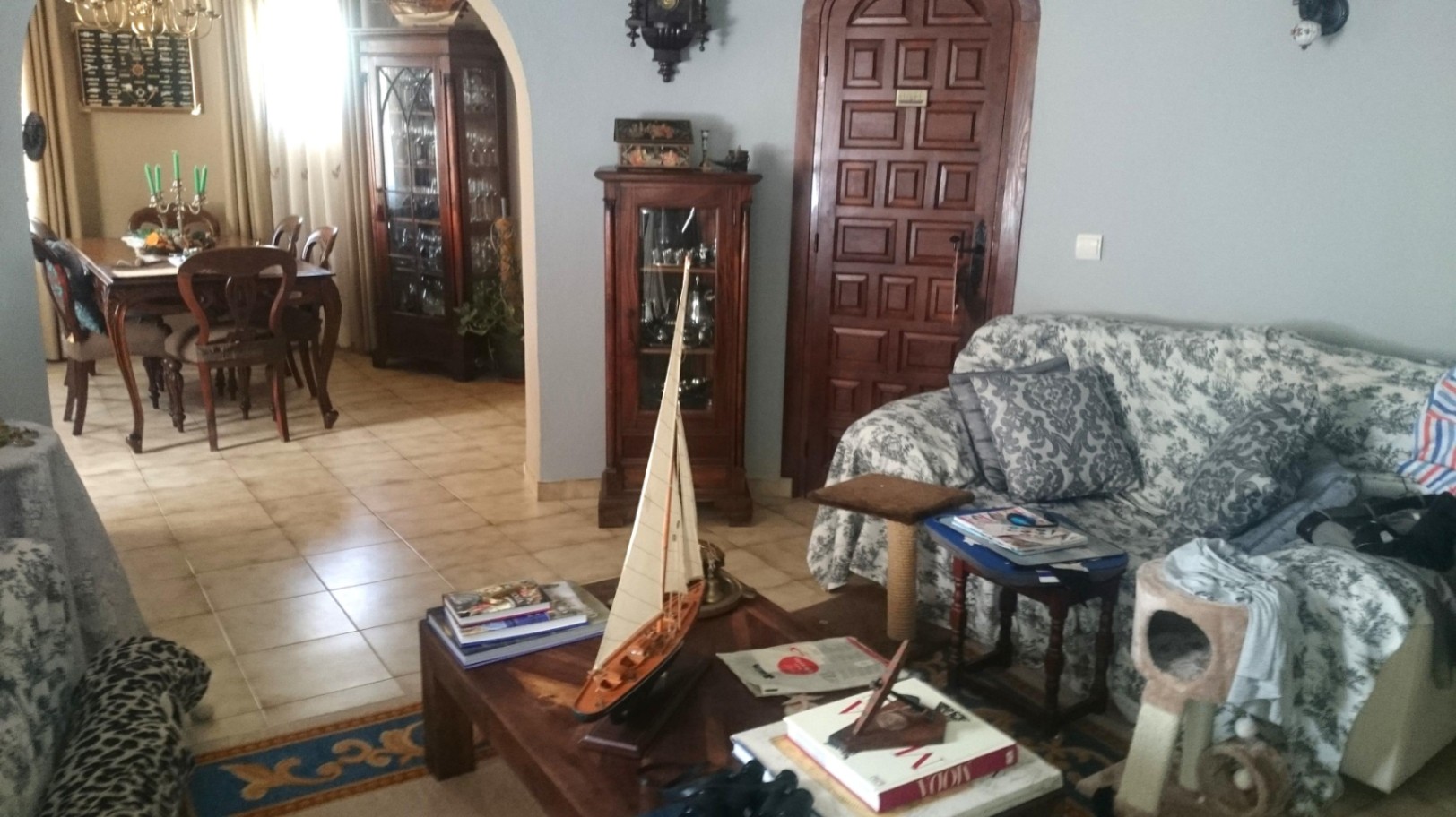 Traditionele woon- en eetkamer met keramische tegelvloer, donkerhouten meubels en een boogvormige doorgang die de ruimtes verbindt.