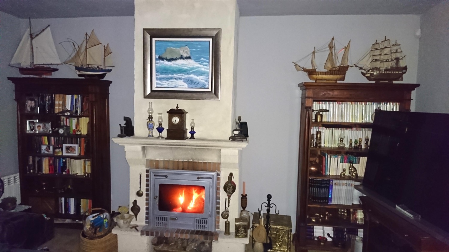 Woonkamer met een stenen open haard voorzien van een houtkachel, geflankeerd door klassieke houten boekenkasten met scheepsmodellen.