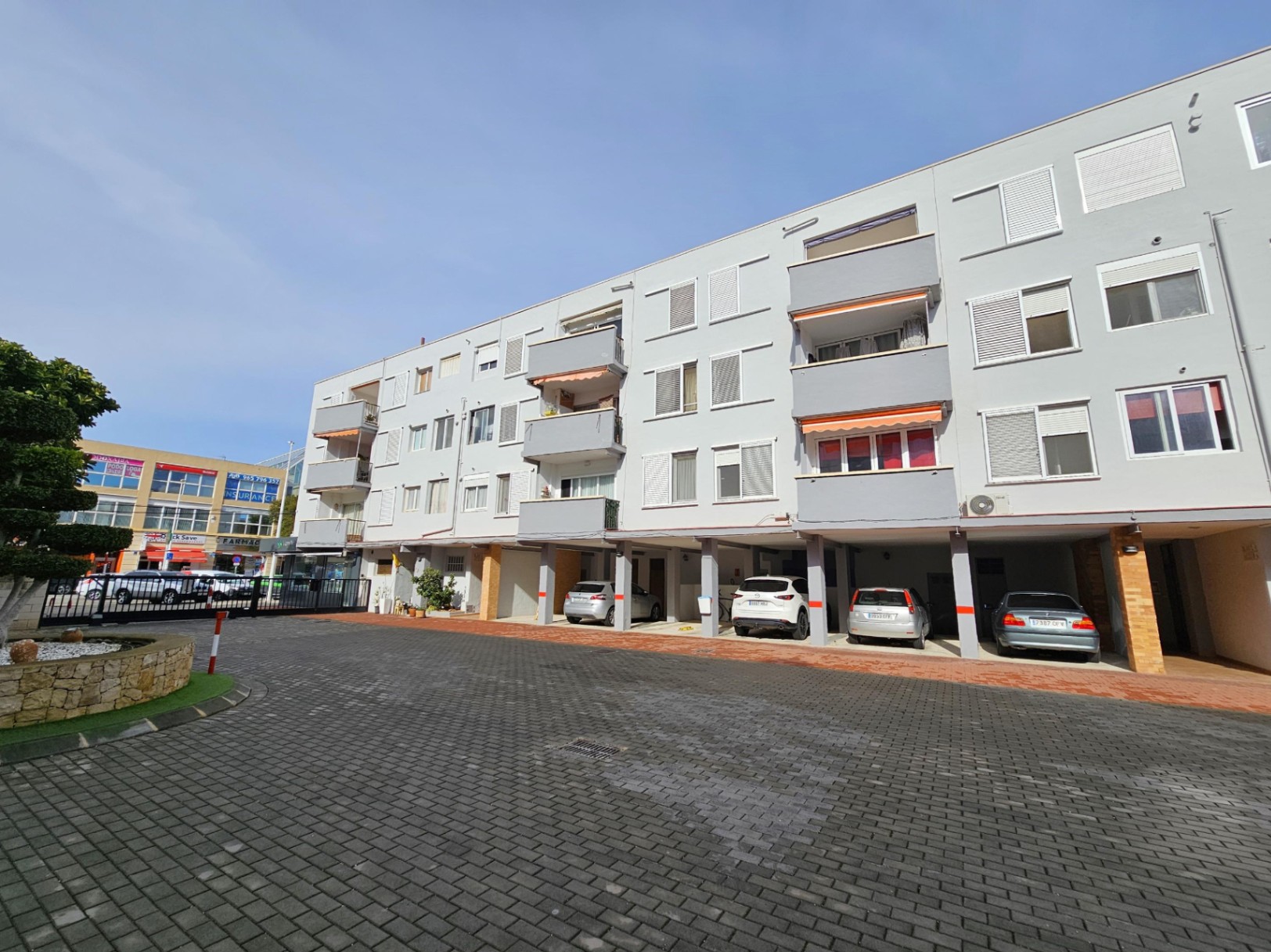 Buitenaanzicht van het appartementencomplex in Jávea met overdekte privéparkeerplaatsen en balkons met oranje zonneschermen.