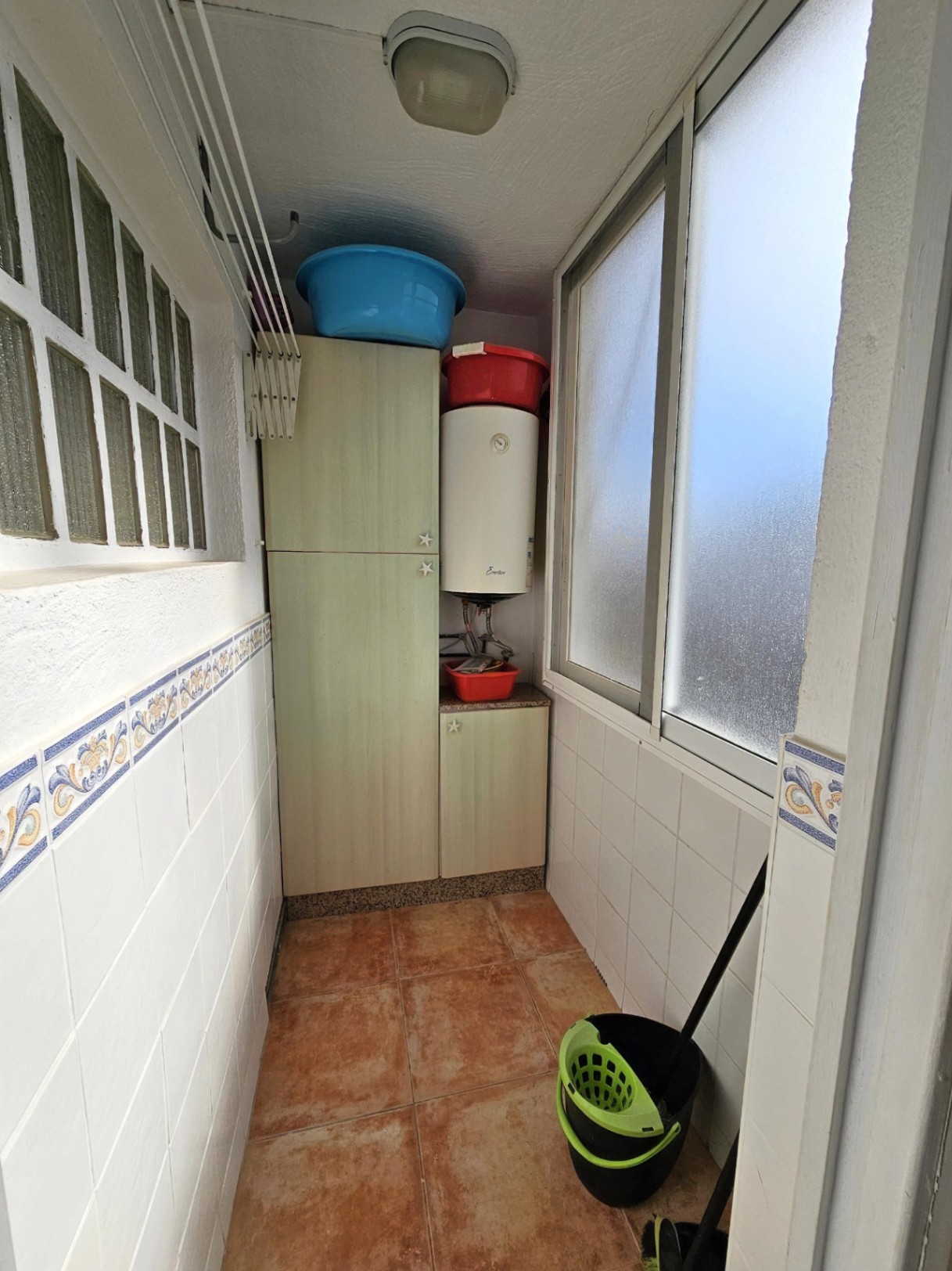 Functionele wasruimte met opbergkasten, elektrische boiler, wanddroogrek en een rustieke tegelvloer.