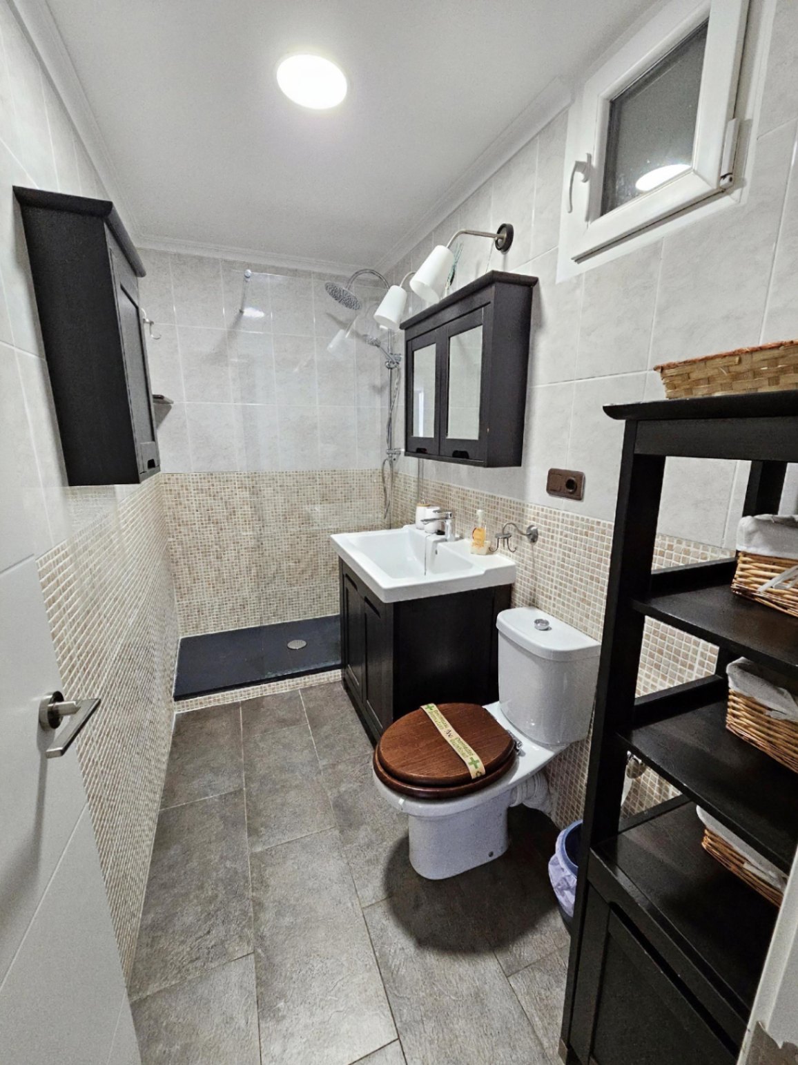 Gerenoveerde badkamer met inloopdouche, mozaïektegels en donkerhouten meubels die zorgen voor een modern en stijlvol contrast.