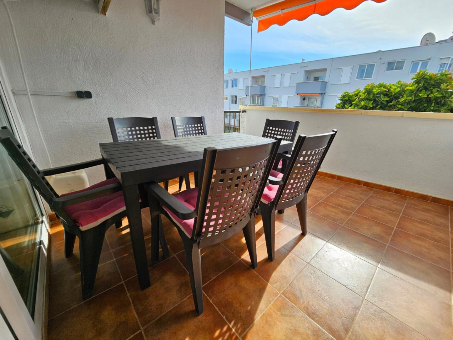 Ruim terras met terracotta vloertegels, voorzien van een eethoek voor buiten en een uitschuifbaar oranje zonnescherm voor extra schaduw.