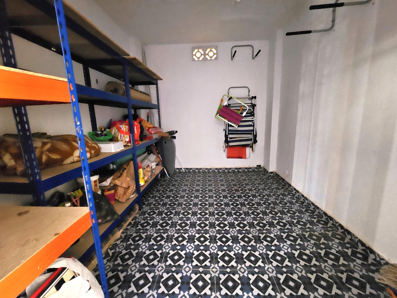 Ruime berging van 12 m² met decoratieve patroontegels, stevige metalen stellingkasten en witte muren voorzien van natuurlijke ventilatie.