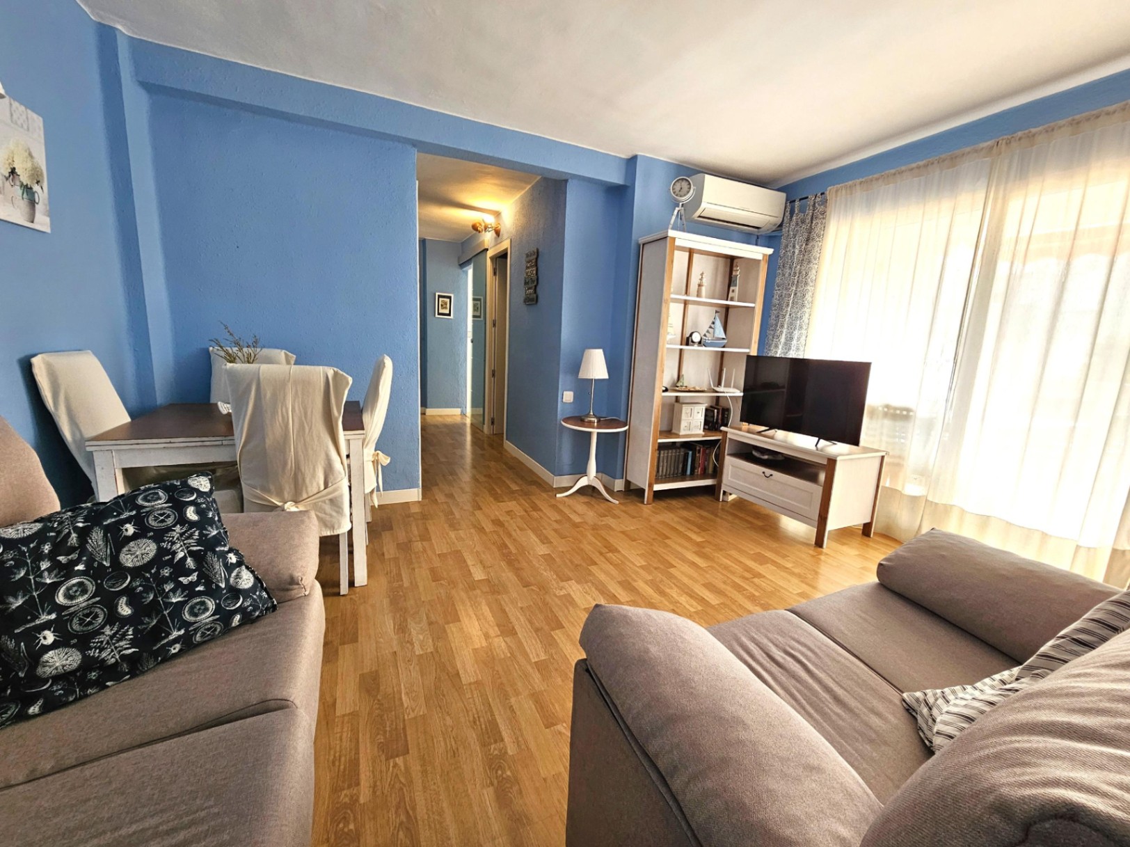 Woon- en eetkamer met blauwe muren, parketvloer, airconditioning en grote ramen die toegang bieden tot het terras.