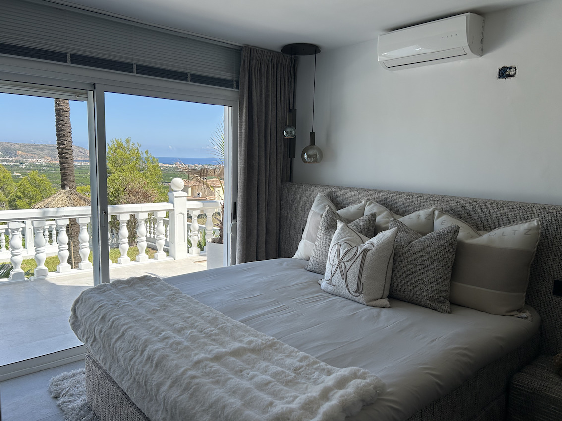 Hoofdslaapkamer met airconditioning en glazen schuifdeuren naar een privéterras. Panoramisch uitzicht over de vallei en de zee vanuit het bed.