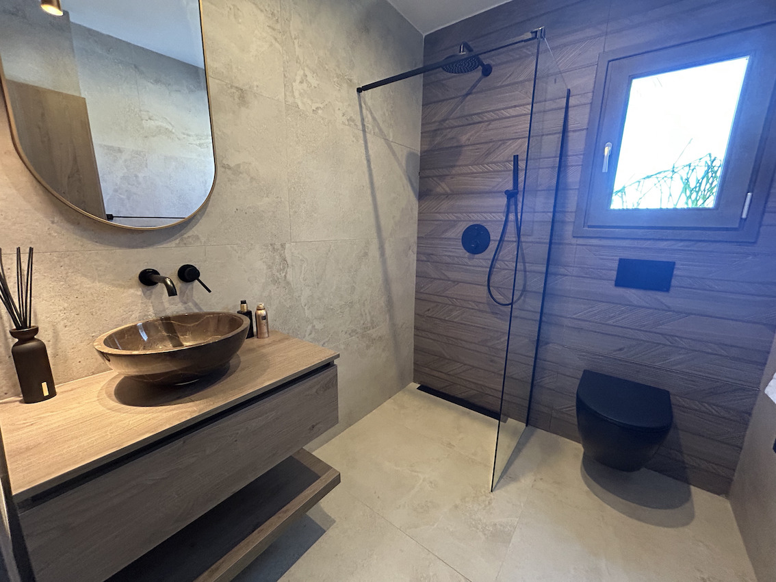 Moderne badkamer met inloopdouche, zwarte kranen, stenen waskom op een zwevend houten meubel en getextureerde wandtegels.