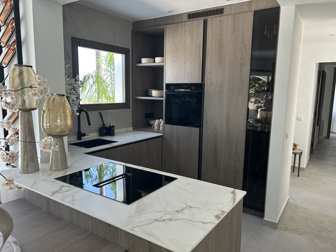 Moderne keuken met marmerlook werkbladen, geïntegreerde inductiekookplaat en donkerhouten kasten. Voorzien van een matzwarte spoelbak en inbouwapparatuur.
