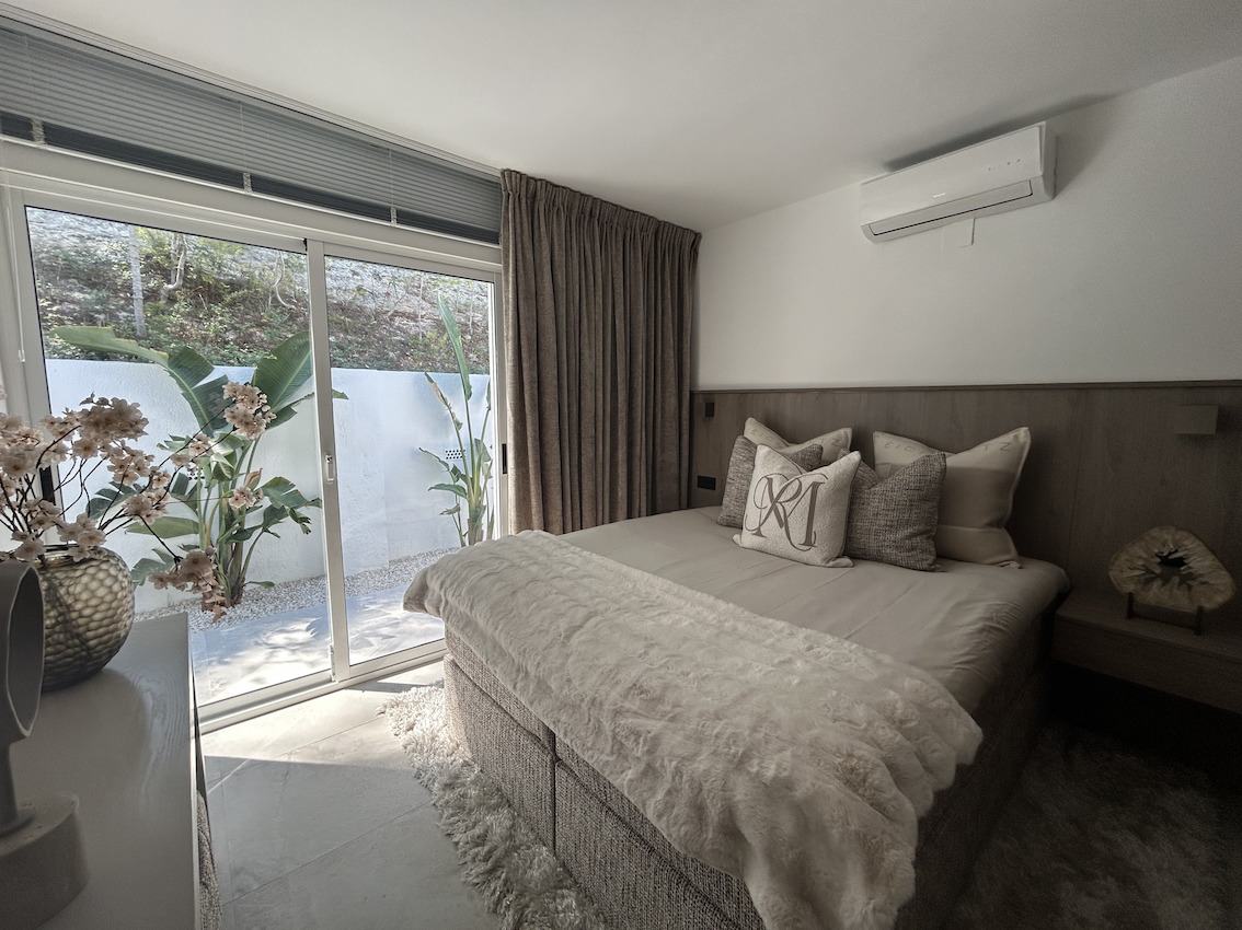 Moderne slaapkamer met directe toegang tot de patio via een schuifpui, voorzien van airconditioning en een houten wandpaneel.