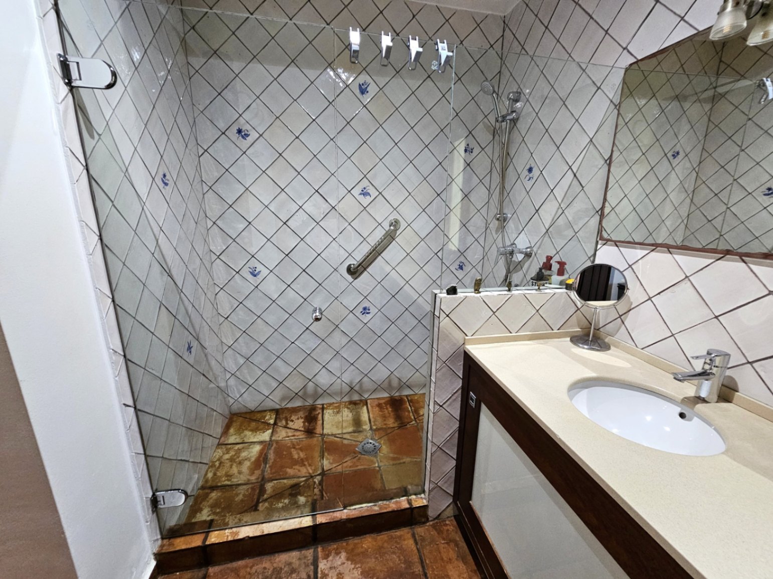 Badkamer met een glazen inloopdouche en handbeschilderde tegels. Voorzien van handgemaakte terracotta vloeren en een wastafelmeubel met een crème werkblad.