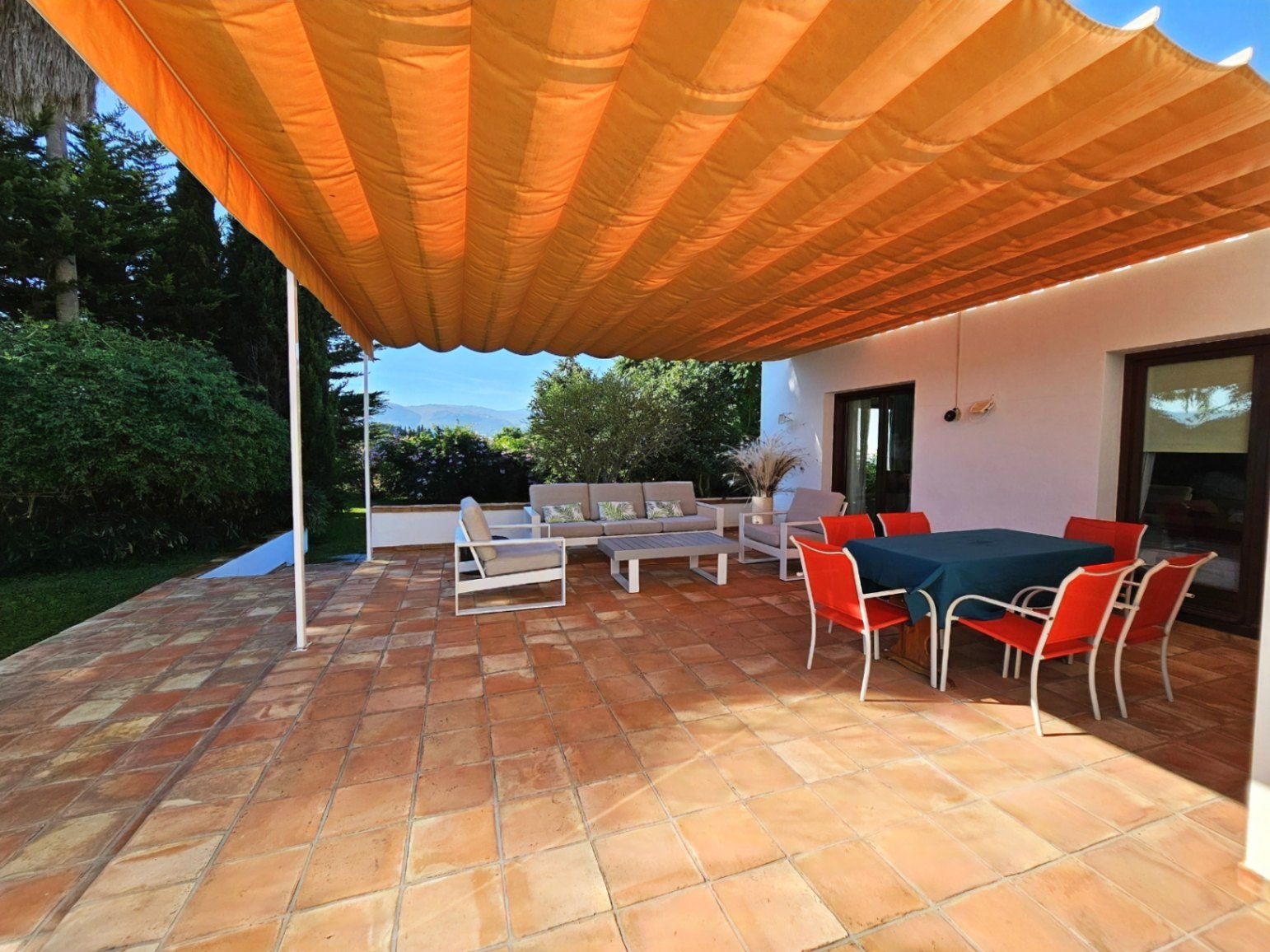 Buitenterras met handgemaakte terracotta tegels, een groot oranje zonnescherm en een eethoek en loungegedeelte in de buitenlucht.